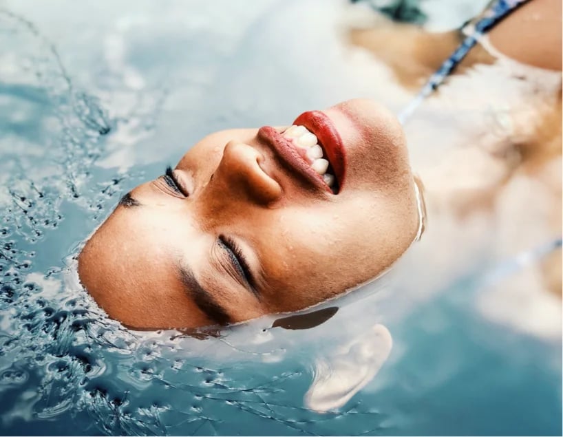 Woman lying face up in the water with her face out of the water.